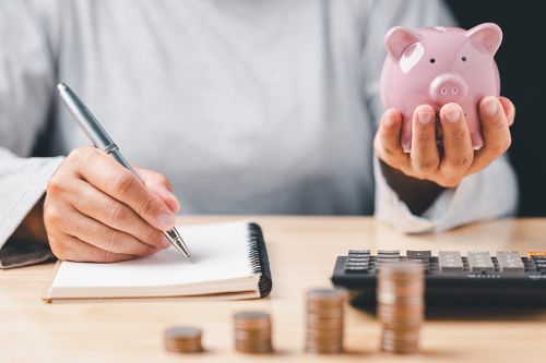Foto: Hand mit Notizbuch und Sparschwein